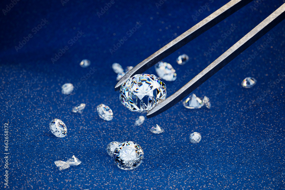 Picking one diamond with a pair of gemstone tweezers. Diamonds on a blue fabric. Picking one diamond with a pair of gemstone tweezers. Diamonds on a blue fabric.
