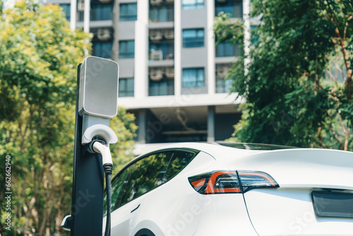 Fototapeta Naklejka Na Ścianę i Meble -  EV electric car charging in green sustainable city outdoor garden in summer. Urban sustainability lifestyle by green clean rechargeable energy of electric BEV vehicle innards