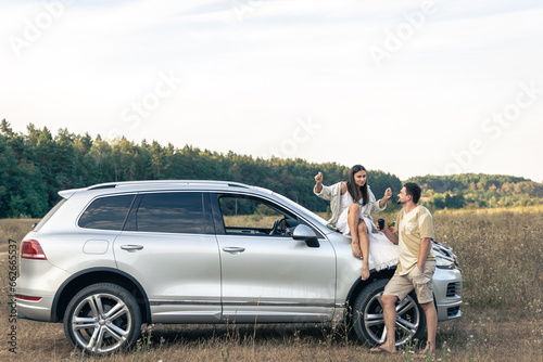 Happy couple enjoy a summer weekend with a car outside the city in a field.