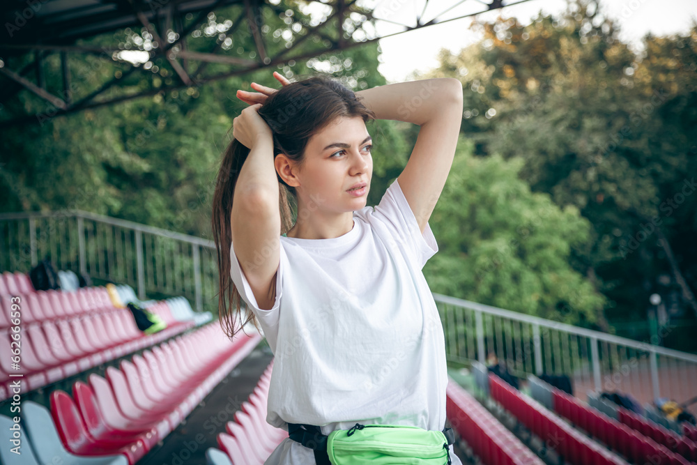 Fototapeta premium Beautiful sporty woman tying hair before her workout at the stadium.