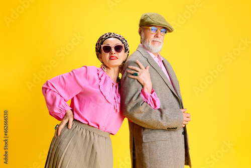 Married couple, elegant woman and handsome man in stylish clothes posing against yellow studio background. Going out for a date. Concept of beauty and fashion, relationship, modern style, age