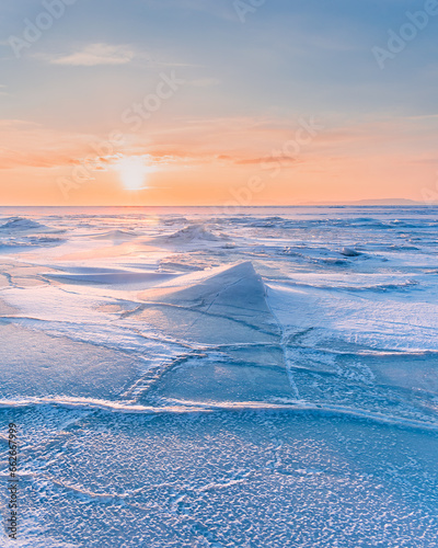 Winter landscape. A frozen surface of ice with snow intersected by many cracks. © Tishina