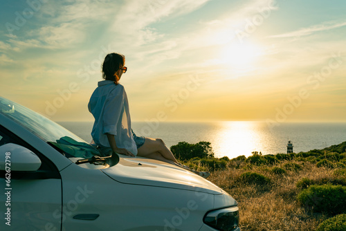 Woman enjoying sunset sitting on car in seashore at sunset, escape from city life