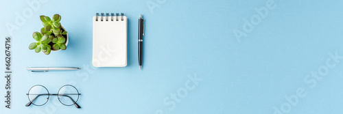 Overhead shot of modern office desktop with business accessories on blue background with copyspace. Flat lay photo