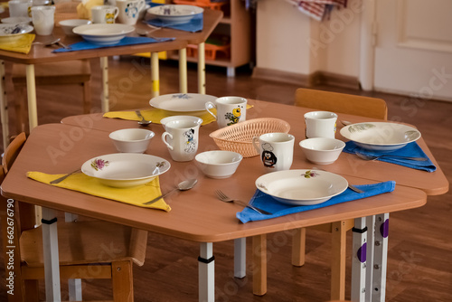 Lunch in kindergarten, on a small table are plates. Meal time in kindergarten. Dining room the wooden chairs and small tables