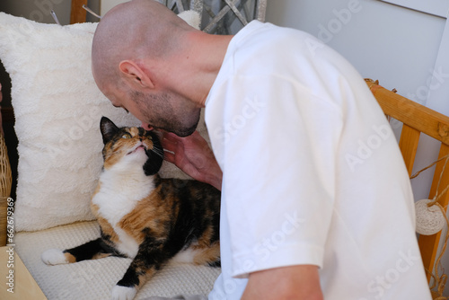 positive charming young man plays with domestic tortoiseshell, chimera cat, stroking four-legged pet, felinotherapy concept, Furry Companion, Family Moment with Cat photo