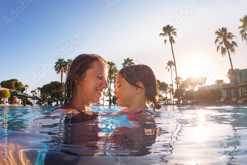 Mother teaching daughter to swim in pool during summer vacation. Mother and daughter playing in water. Beach resort vacation by the sea. Winter or summer seaside holiday.
