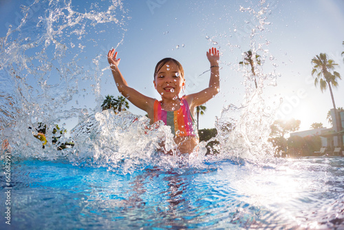 Little girl splashing water in the pool, playing in the water, having fun. Beach resort vacation by sea. Winter or summer seaside resort holiday.