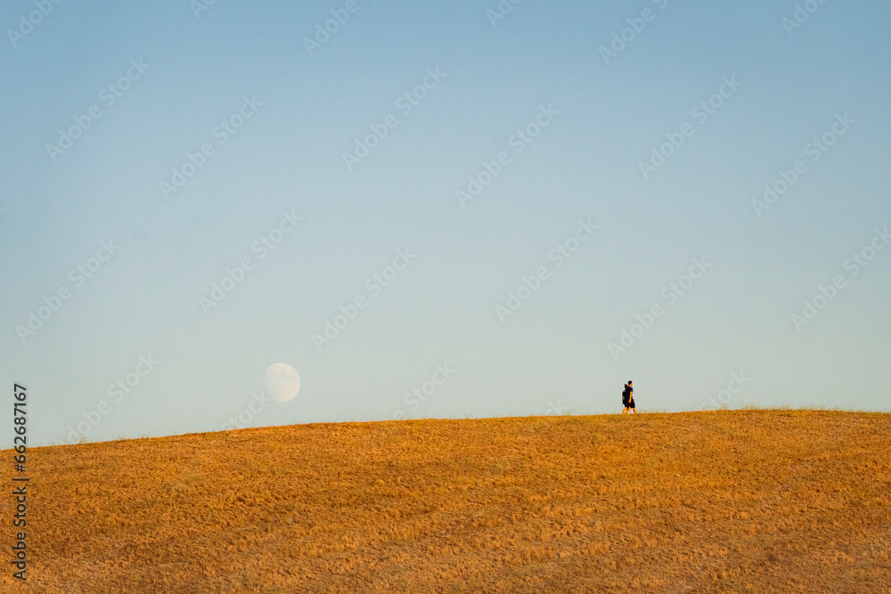 coppia passeggia su collina con dietro enorme luna crescente - obrazy, fototapety, plakaty 