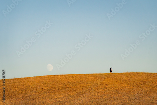 coppia passeggia su collina con dietro enorme luna crescente photo
