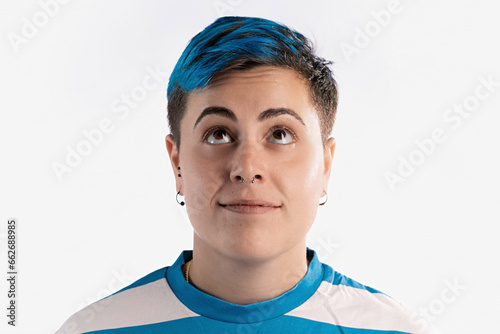 Half-length portrait of a gender fluid woman with vibrant blue short hair on a white background. She exudes a curious demeanor, looking upwards with an inquisitive expression.