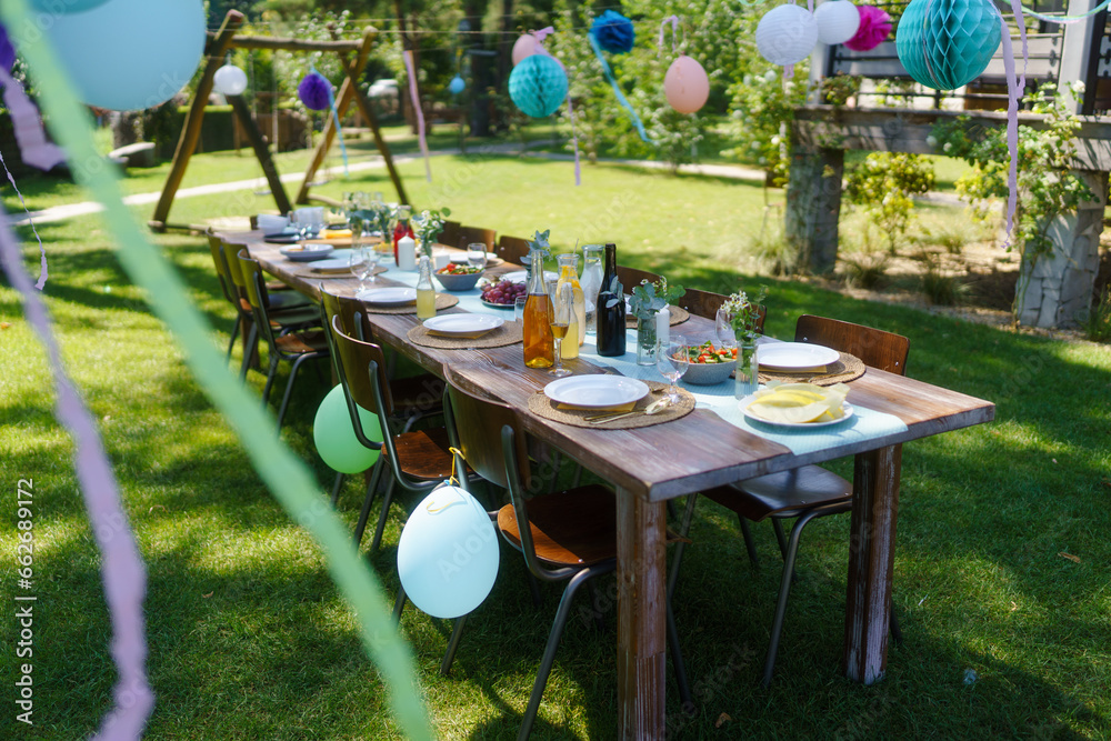 Set table for summer garden party. Table setting with glasses, fruit lemonade, fresh fruits and salads and delicate floral decoration. Colorful paper decorations for party.