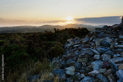At the side of a large cairn built on Llanbedrog Headland in Llanbedrog as the sun sets over a distant Snowdonia. photo