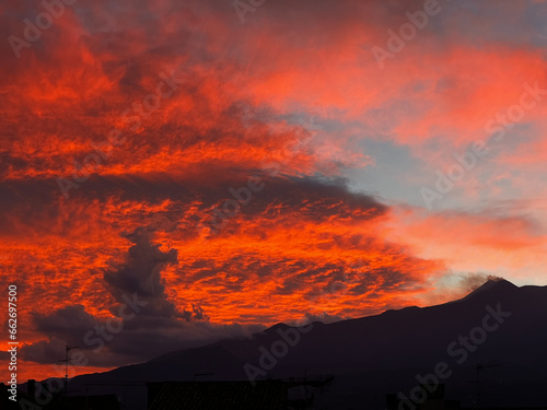Tramonto del sole dietro il cratere del vulcano Etna, che rende al crepuscolo le nuvole di un colore rosso acceso