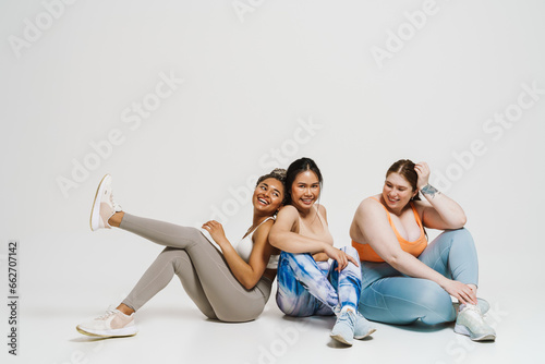 Fototapeta Naklejka Na Ścianę i Meble -  Group of joyful women in sportswear posing together while sitting isolated over white wall