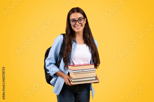 Happy teen student lady with backpack in glasses hold many books, enjoy study