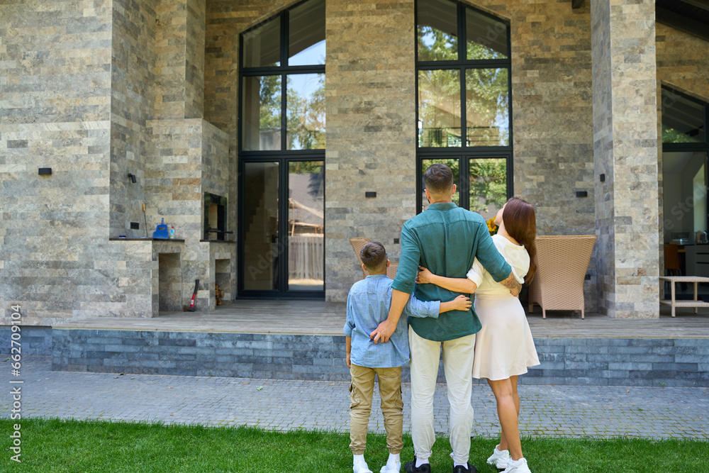 Happy family stands hugging on lawn in front of country house