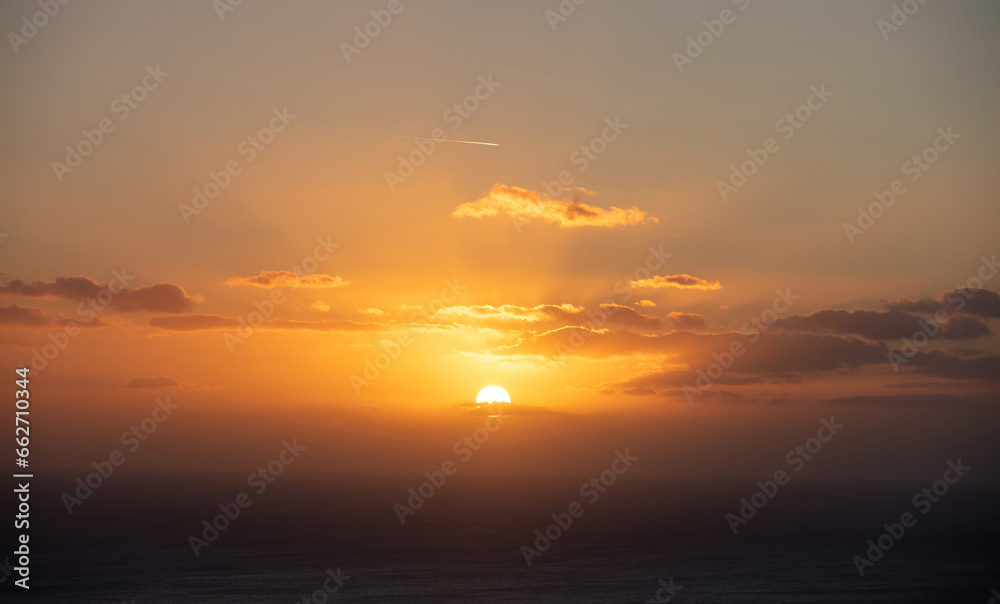 Sunset through and behind the cloud over the sea background. Sunbeam colors golden the sky