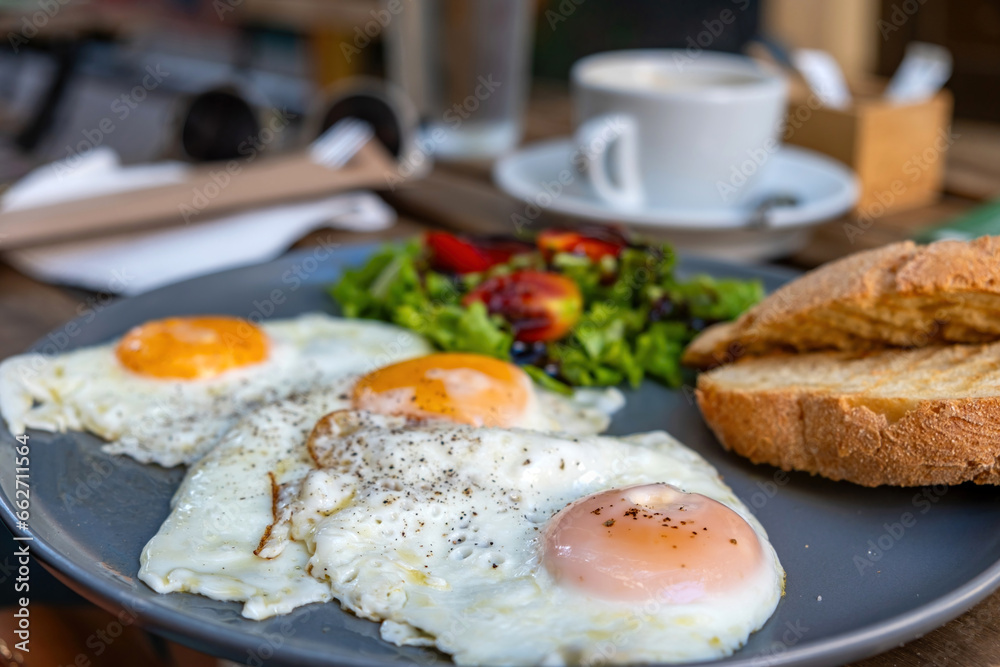 Fried egg with pepper, salad, toasted bread in dish and a blur cup of coffee on wooden table. Fried egg with pepper, salad, toasted bread in dish and a blur cup of coffee on wooden table.