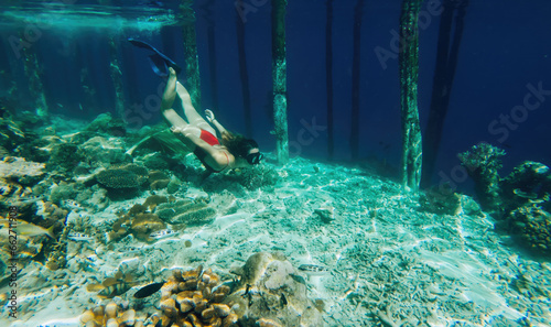 Young girl in snorkeling mask dive underwater to see tropical fishes in coral reef sea pool,