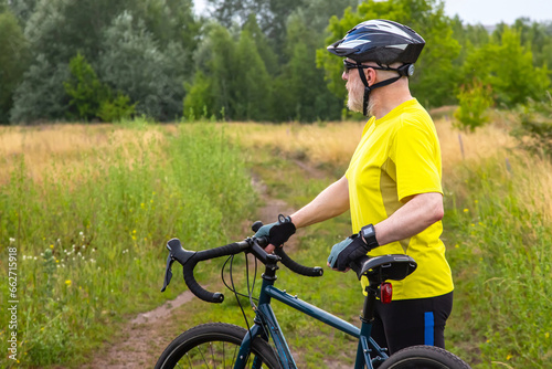 Fototapeta Naklejka Na Ścianę i Meble -  bearded man cyclist in yellow clothes is resting on a bicycle on the road in nature. sports, hobbies and entertainment for health