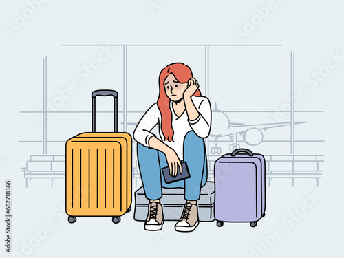 Upset woman airport passenger sits among tourist suitcases and waits for plane that is late due to bad weather. Concept of flight cancellation causing inconvenience to airport passengers