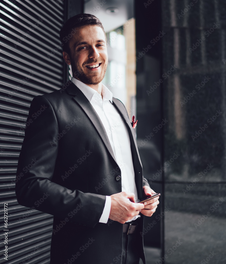 Fototapeta premium Pleasant man in classical suit with smartphone looking at camera with smile in street in downtown