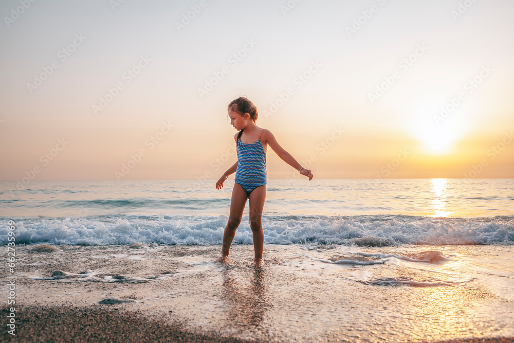 The child happily plays in the waves on the seashore. A girl in a blue swimsuit laughs while playing in the waves on the beach