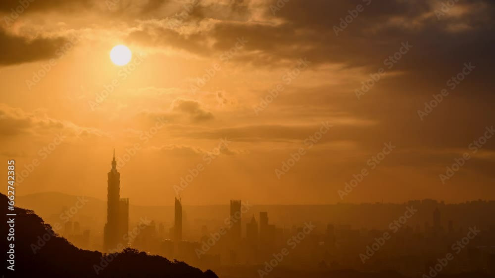 At dusk, the sun breaks through the clouds and shines on Taipei City. Silhouettes of city buildings. Orange sky and dark clouds.