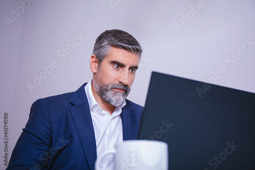 Close up portrait of adult businessman executive sitting at desk using laptop