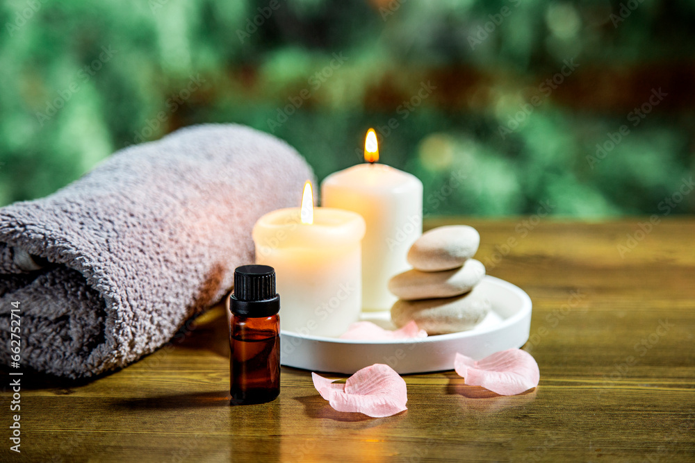 spa still life with candles, towel and essetial oil against green nature background on wooden table spa still life with candles, towel and essetial oil against green nature background on wooden table