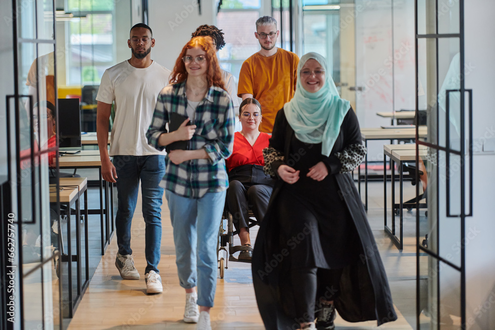 Fototapeta premium A diverse group of business people walking a corridor in the glass-enclosed office of a modern startup, including a person in a wheelchair and a woman wearing a hijab, showing a dynamic mix of