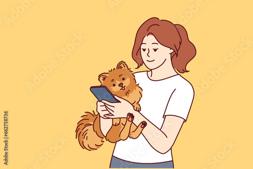 Woman has small dog and phone in hands  and is looking on internet for hotel or cafe to relax with pet. Caring girl with dog calls veterinarian to make appointment for vaccinations
