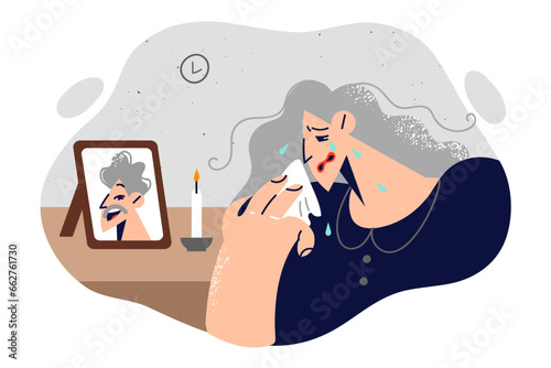 Widow woman is crying standing near portrait of deceased husband and wiping tears from face