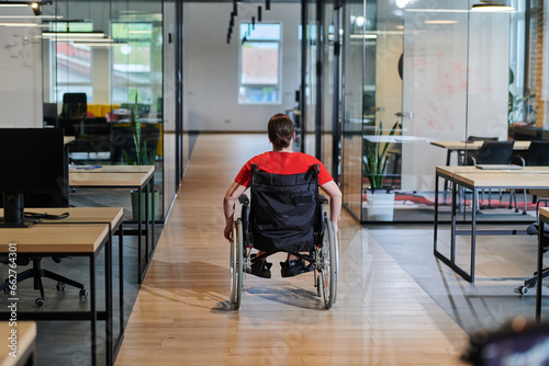 A modern young businesswoman in a wheelchair is surrounded by an inclusive workspace with glass-walled offices, embodying determination and innovation in the business world