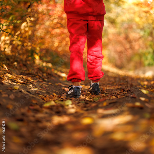 Back view of the legs of a boy walking through a park. A boy in a red suit in a park in the fall.