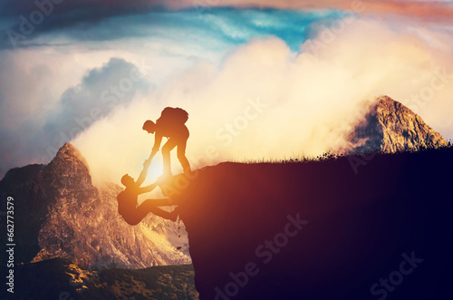 Man giving his hand to help his friend climb up the mountain photo
