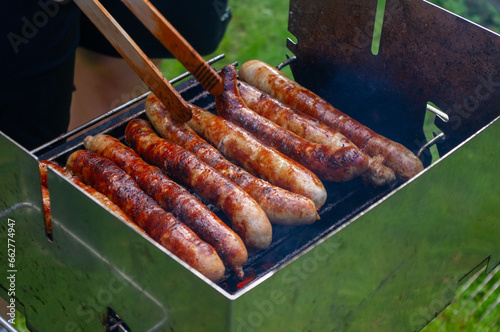 Person grillt Bratwürste auf einem Grill mit einer Grillzange