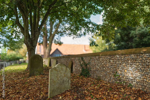 Shallow focus of very old stone work gravestone seen during early autumn. A carpet of dead leaves carpets the area. Seen next to an ancient flint wall. photo