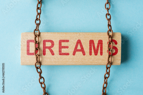 Wooden block with word Dreams is held by metal chain. Concept of realizing dreams and overcoming obstacles