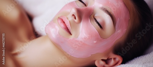 Beautiful young girl getting a pink facial mask at an indoor spa salon With copyspace for text