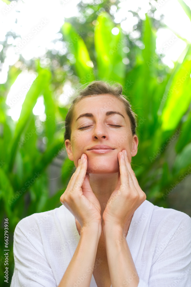 Vertical portrait of a middle-aged woman doing a facial massage and smiling. Self-facial massage and daily skin care in adulthood. Organic cosmetics for face care. Vertical portrait of a middle-aged woman doing a facial massage and smiling. Self-facial massage and daily skin care in adulthood. Organic cosmetics for face care.