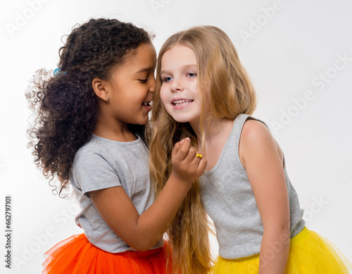 two little smiling girls with different complexion gossiping isolated on white background photo