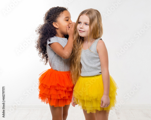 two little smiling girls with different complexion gossiping isolated on white background photo