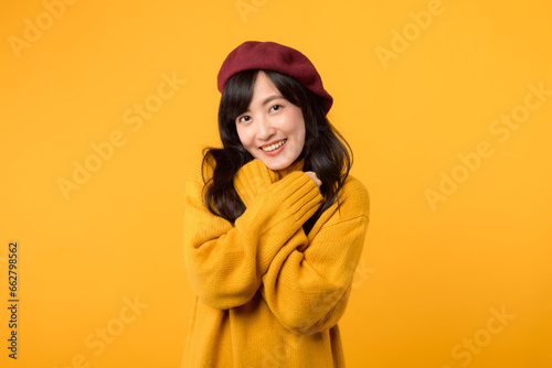 Confident young Asian woman in her 30s, crossing her arms with a cool and stylish expression, donning a yellow sweater and red beret against a yellow background.