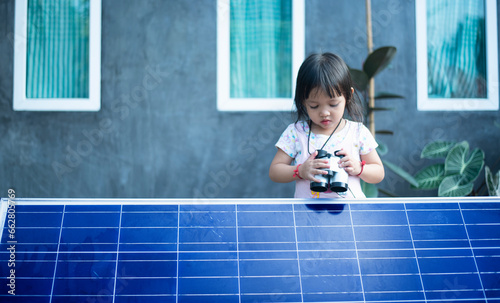 Happy Asian girl admiring solar panels with binoculars recently installed at home.