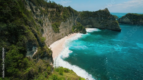 White sandy Diamond beach on Nusa Penida Bali Indonesia. Ocean waves splash on rocky coastline with sheer cliff.
