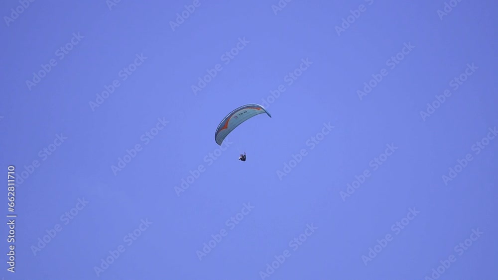 An adrenaline-pumping extreme sport, paragliding against the clear blue sky. Paraglider flying with his parachute above the sky with a background of blue sky and white clouds in a sunny day. An adrenaline-pumping extreme sport, paragliding against the clear blue sky. Paraglider flying with his parachute above the sky with a background of blue sky and white clouds in a sunny day.