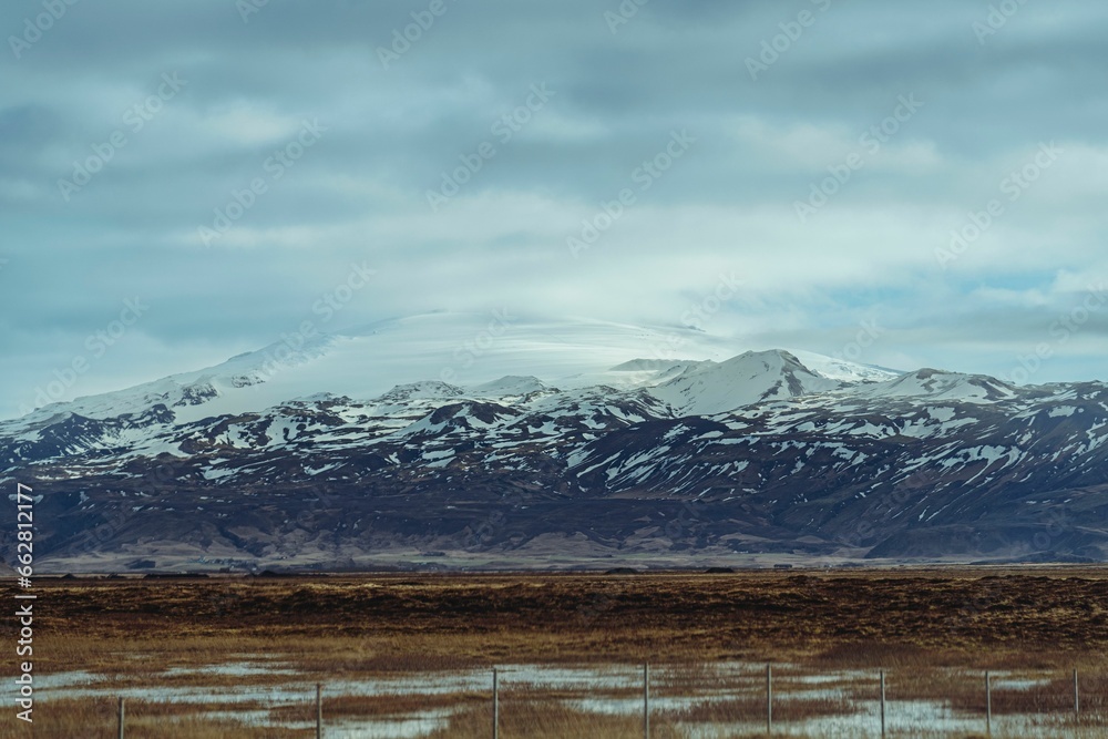 a view of snow on mountains behind a fence and grassy field, Iceland