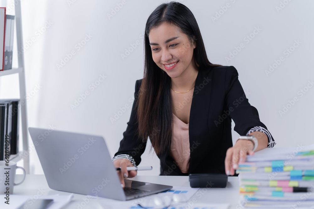 Sharing good business news. Attractive young businesswoman talking on the mobile phone and smiling while sitting at her working place in office and looking at laptop PC. Sharing good business news. Attractive young businesswoman talking on the mobile phone and smiling while sitting at her working place in office and looking at laptop PC.